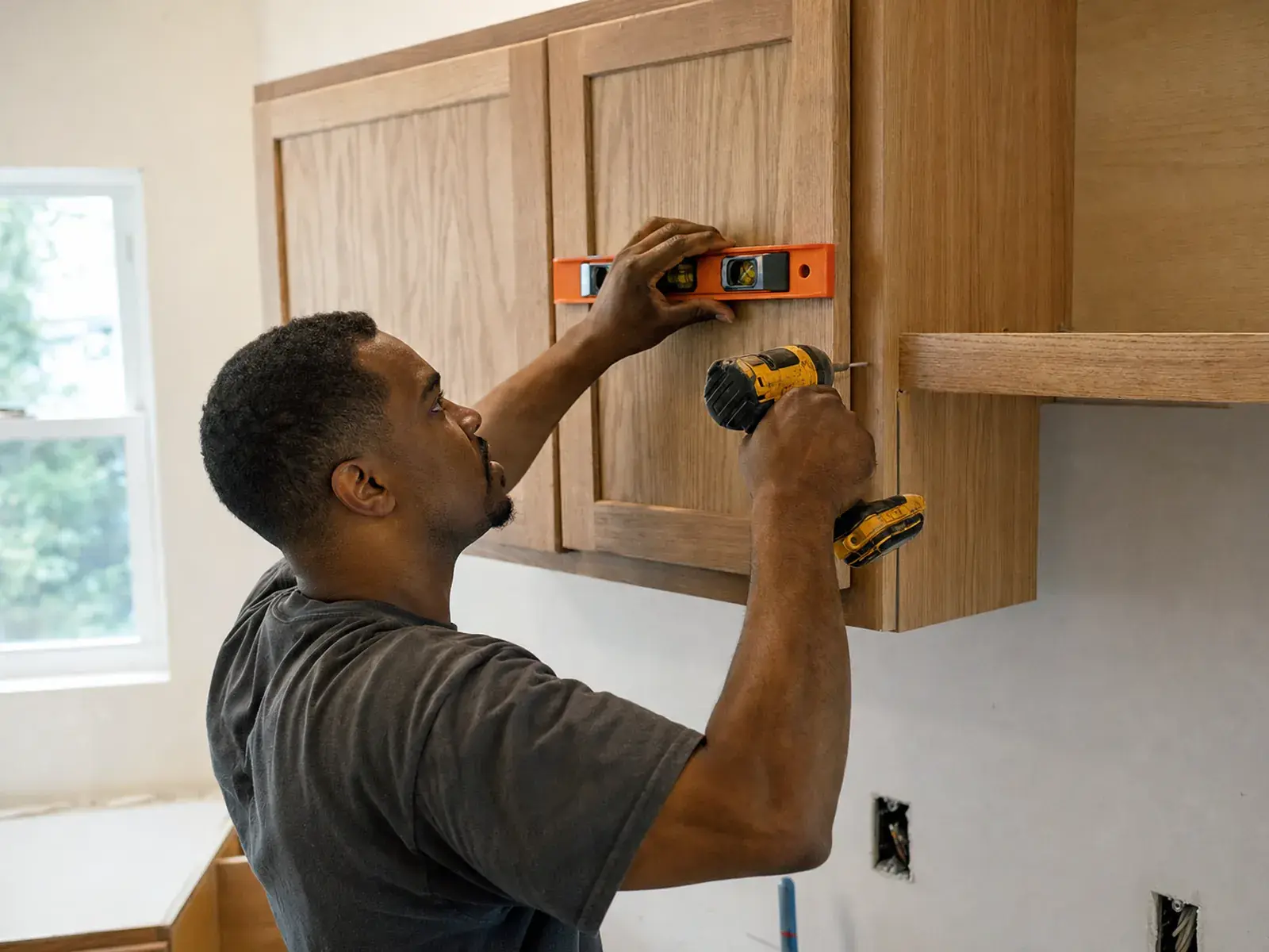 Un remodelador nivelando e instalando gabinetes superiores de cocina